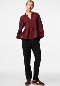 Bordeaux, tekstureret bluse med bred udskæring og flagrende ærmer, parret med sorte bukser og bordeaux sneakers, sat mod en hvid baggrund.