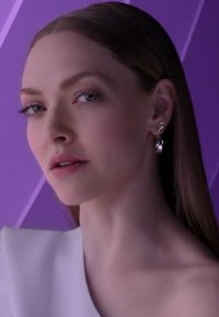 Zbliżenie osoby o prostych, brązowych włosach, noszącej srebrne kolczyki koła i biały top, na tle fioletowego, paskowanego tła.