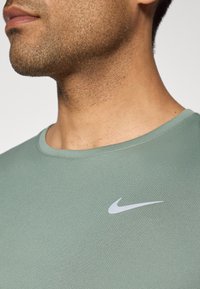 Close-up mehe kaelast ja alumisest näost, kerge habemejoonega, seljas helesinine särk, mille rinnaosas on valge Nike logo.