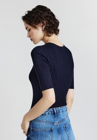Body in cotone navy a coste con maniche corte, caratterizzato da un collo rotondo e una forma aderente, abbinato a pantaloni corti in denim azzurro a vita alta.