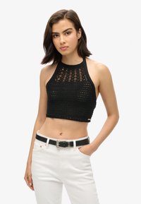 Top corto negro de ganchillo con un patrón de tejido abierto, combinado con unos vaqueros blancos de cintura alta y un cinturón negro con una hebilla decorativa.