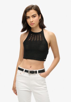 Zwarte gehaakte halter crop top met een open geweven patroon, gecombineerd met hoge witte spijkerbroeken en een zwarte riem met een decoratieve gesp.