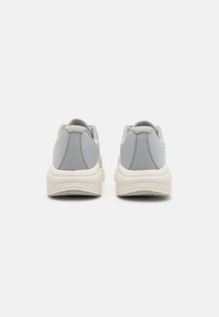 Baskets de sport grises avec une tige texturée, un bout rond et une semelle de couleur crème. Comprend un col rembourré et un panneau arrière lisse.