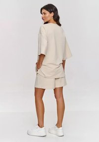 Beżowy, oversize t-shirt z krótkim rękawem, zestawiony z pasującymi szortami. Oba wykonane są z miękkiego materiału. Całość dopełniają białe sneakersy.