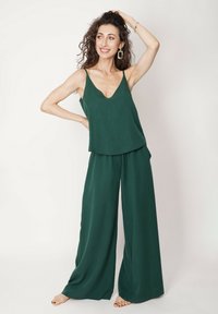 Zielona, bezrękawnikowa bluzka z dekoltem w serek, zestawiona z szerokimi spodniami. Gładka tekstura, luźny krój i miękki spad. Minimalistyczny design.