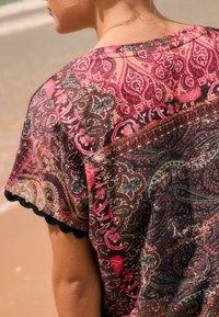 Šarena, uzorčena majica s paisley uzorcima u nijansama ruži�časte, crne i tirkizne; kratki rukavi s valovitim rubovima; lagana tkanina.