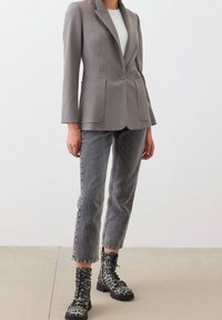 Šedé na míru šité sako se dvěma předními kapsami, kombinované se šedými džíny a černými bojovými botami s leopardím potiskem, které mají šněrování vpředu a masivní podrážky.