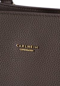 Barna, textúrázott bőr, varrási részletekkel, arany névtáblával, melyen a "CARLHEIM" és a "COPENHAGEN" felirat van bélyegezve. Nagyított nézet.