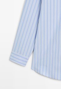 Hellblau gestreiftes Hemd mit weißen vertikalen Streifen, ausgestattet mit einem umgeschlagenen Manschetten und glatter Textur. Abgerundeter Saum am unteren Rand.