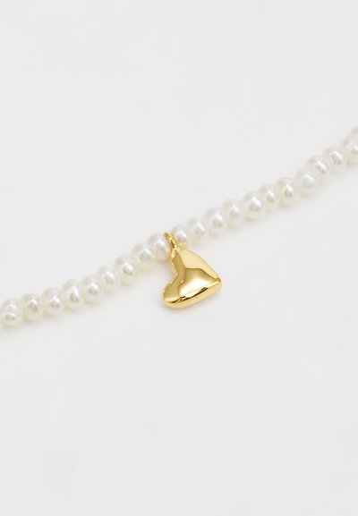 Perlehalssmykke med små, runde hvide perler og en skinnende guld hjerteformet charm som centralt accent.