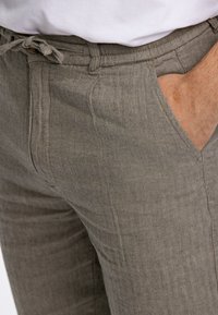 Pantalons en chevrons gris clair en tissu texturé, dotés d'une taille à cordon de serrage, de poches latérales et d'une coupe slim.