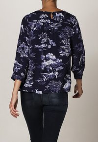 Blusa navy con stampa botanica bianca, caratterizzata da un'apertura a chiave nella parte posteriore e maniche a ¾, realizzata in tessuto leggero.