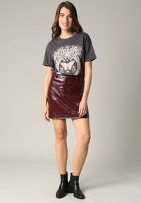 Camiseta gráfica gris con patrones de flores y mariposas, combinada con una minifalda de cuero burdeos brillante y botas negras hasta el tobillo.