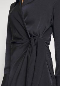 Gros plan d'une robe portefeuille noire à manches longues avec un nœud en tissu noué à la taille.