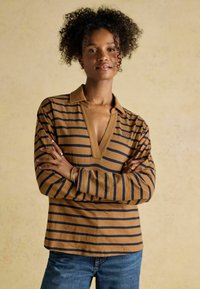 Pika-pikkade varrukatega pruun triibuline särk V-kaelusega ja siniste triipudega. Kangas näib olevat pehme, mugava lõikega ja silmatorkavate õmbluse detailidega.