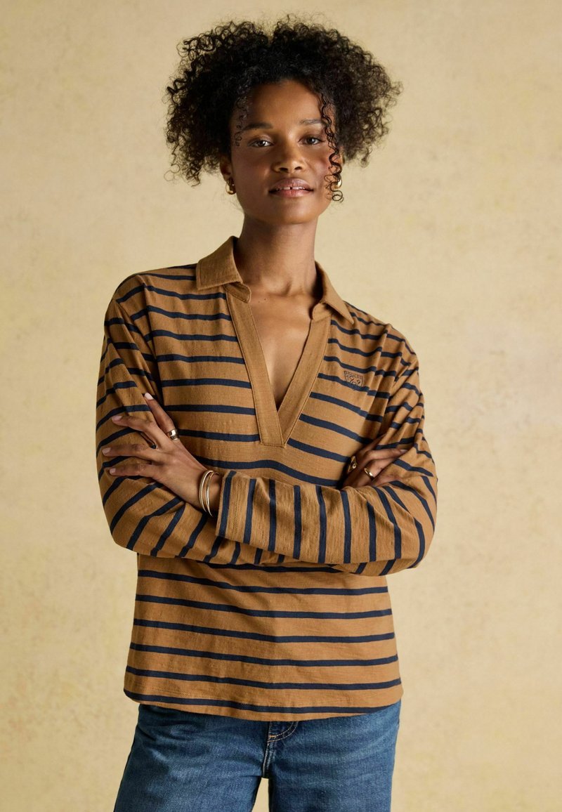 Pika-pikkade varrukatega pruun triibuline särk V-kaelusega ja siniste triipudega. Kangas näib olevat pehme, mugava lõikega ja silmatorkavate õmbluse detailidega.