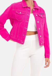 Varm pink denimjakke med klassisk design, to brystlommer og sølvfarvet hardware. Båret over en hvid ribbet top og højttaljede nederdele.