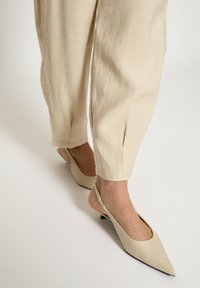 Beežid slingback-kingad terava varbaga, valmistatud siledast materjalist, kombineeritud heledate beežide, tekstuursete, lahtise sobivusega pükstega.