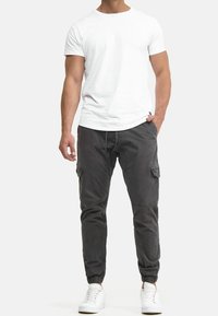 Weißes kurzärmliges T-Shirt kombiniert mit dunkelgrauen Cargo-Hosen mit elastischen Bündchen und mehreren Taschen, vervollständigt mit weißen Turnschuhen.