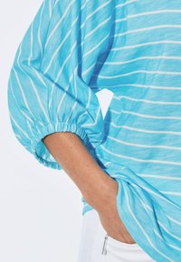 Himmelblaue gestreifte Bluse mit lockeren, puffartigen Ärmeln, elastischen Bündchen und einem entspannten Schnitt. Weiche Textur mit weißen horizontalen Streifen.