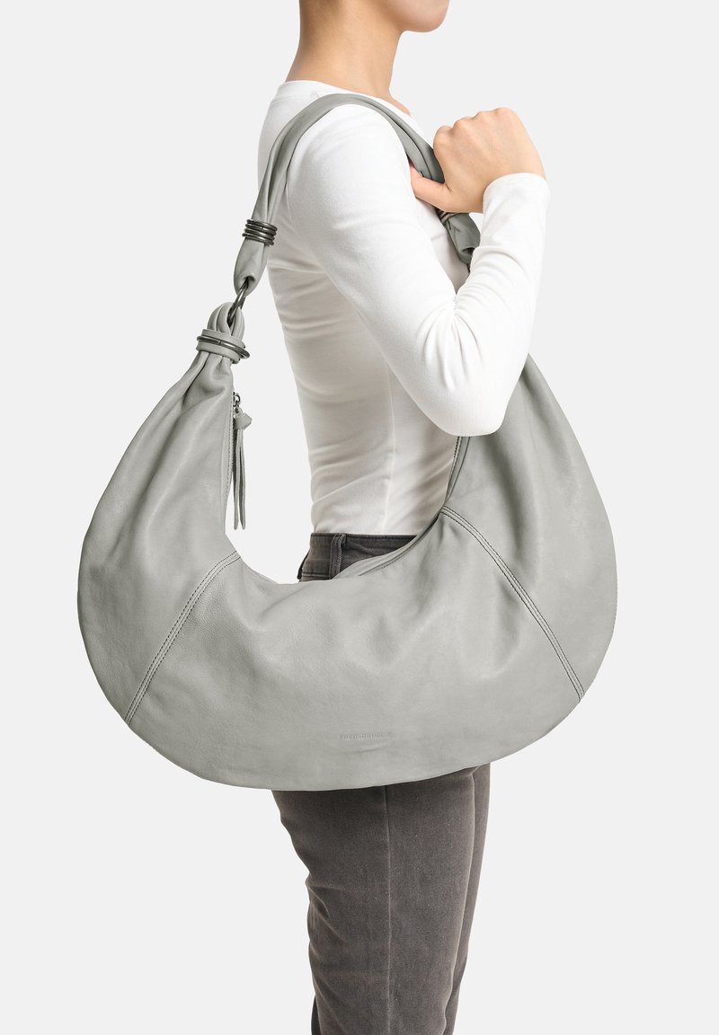 Sac à bandoulière en cuir gris de forme croissante, texture lisse, détails de sangle nouée et surpiqûres contrastantes. Fermeture éclair incluse.