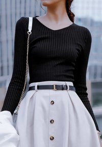 Zwarte ribgebreide longsleeve top gecombineerd met een witte rok met knopen en een zwarte riem met een gouden gesp. Ketting schoudertas zichtbaar.