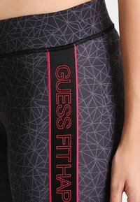 Tajta leggings gjorda av texturerat tyg med ett geometriskt mönster, med ett brett svart band med "GUESS FIT" i röd skrift.