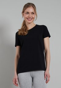 Black cotton T-shirt with short sleeves, round neckline, and a relaxed fit, paired with gray sweatpants. Smooth texture and simple design.