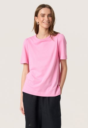 Lys pink kortærmet t-shirt lavet af blødt bomuld med rund halsudskæring og let puffede ærmer, parret med løse sorte shorts.