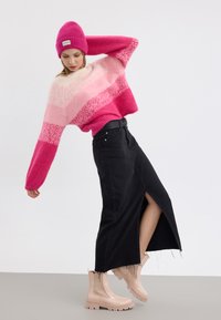 Gestreifter, gestrickter Pullover in Pink und Creme, schwarzer Jeansrock mit Schlitz an der Seite und beiger Knöchelstiefel mit klobigen Sohlen.