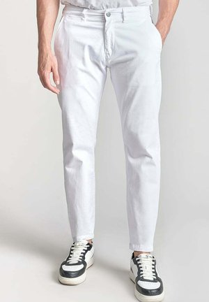 Pantalons en coton blancs avec une coupe droite, design à cinq poches, fermeture éclair et bouton à l'avant, associés à des baskets noires et blanches.