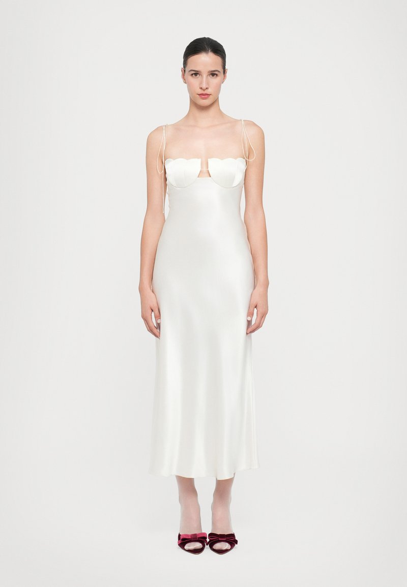 Vestido de satén blanco con detalle de busto en forma de corazón y tirantes finos. Silueta ajustada y elegante con un dobladillo de longitud media. Combinado con tacones burdeos.