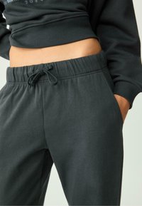 Donkergrijze sweatpants gemaakt van zacht materiaal, met een elastische tailleband met een trekkoord, zijzakken en een ontspannen pasvorm.