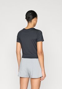 Μαύρο κοντομάνικο μπλουζάκι από λείο ύφασμα, σε συνδυασμό με σορτς σε ανοιχτό γκρι χρώμα. Το μπλουζάκι έχει στρογγυλή λαιμόκοψη και cropped μήκος.