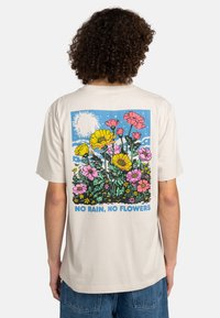 Cream-colored cotton t-shirt featuring a colorful floral graphic on the back, with text "NO RAIN, NO FLOWERS" at the bottom.