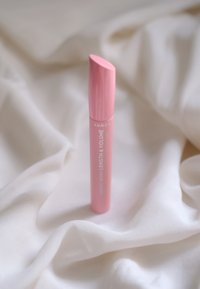 Lyserød mascara tube med en rund kapsel, prydet med hvid tekst, der står "LUMENE NORDIC BERRY LENGTH & VOLUME" på en hvid stofbaggrund.