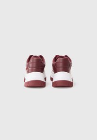 Une paire de baskets bordeaux et blanches avec des semelles épaisses, vue de l'arrière sur un fond clair.