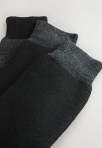 Calcetines negros y grises con puños acanalados. El material parece suave y texturizado, con diferentes tonos que van del gris oscuro al claro.