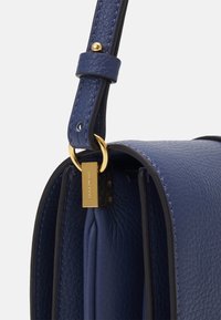 Borsa a mano in pelle blu con finitura testurizzata. Dotata di un accessorio dorato e di una forma strutturata. Tracolla regolabile fissata con anelli.