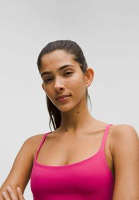 Cămașă fără mâneci, de culoare roz, cu bretele subțiri, având o textură netedă și un design ajustat. Formă simplă, stil minimalist, fără modele sau embellismente.