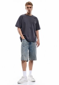 Grå oversized t-shirt lavet af blødt stof, parret med lyse denim shorts. Modellen bærer hvide sneakers og sokker til midten af læggen.