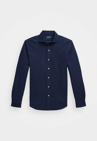 Jūrinės mėlynos spalvos ilgomis rankovėmis marškiniai su mygtukais, pagaminti iš medvilnės, turi klasikinį apykaklę, baltus mygtukus ir subtilų išsiuvinėtą logotipą ant krūtinės.