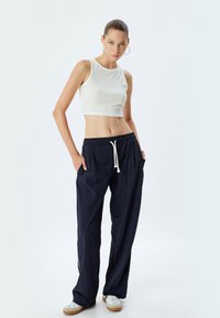 Korstret hvid ribbet tanktop parret med løstsiddende marineblå træningsbukser med elastisk talje og snøre, båret med hvide sneakers.
