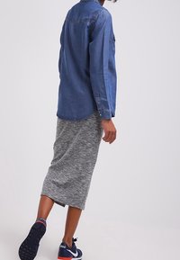 Camicia di jeans con colletto, maniche lunghe e vestibilità rilassata, abbinata a una gonna midi grigio mélange e scarpe sportive nere.