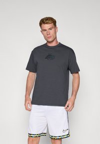 Grå t-shirt med korte ærmer og en sort 'Lakers' logo, sammen med hvide basketballshorts med en farverig mønstret kant og Nike-logo.