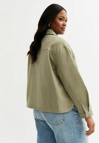 Chaqueta verde oliva con un ajuste relajado, puños de botón y dobladillo recto. Tejido texturizado, costura trasera única y diseño de cuello clásico.