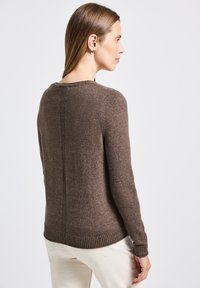 Brun stickad tröja med rund halsringning, ribbade ärmslut och nederkant. Har en vertikal sömdetalj på baksidan. Bärs med ljusa byxor.