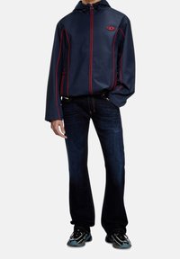 Granatowy wiatrówka z czerwoną lamówką, z zamkami błyskawicznymi, kieszeniami oraz kapturem, zestawiona z ciemnoniebieskimi dżinsami oraz czarnymi tenisówkami z niebieskimi akcentami.