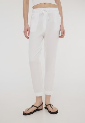 Pantaloni jogger bianchi, larghi, con elastico in vita e cordino, dotati di tasche laterali e polsini elastici alle caviglie.