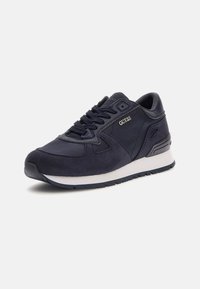 Tumesinine sneakers, millel on sujuvate ja tekstuursete materjalide segu, valge vahekiht, must tallavari ja metallist logo aksent.
